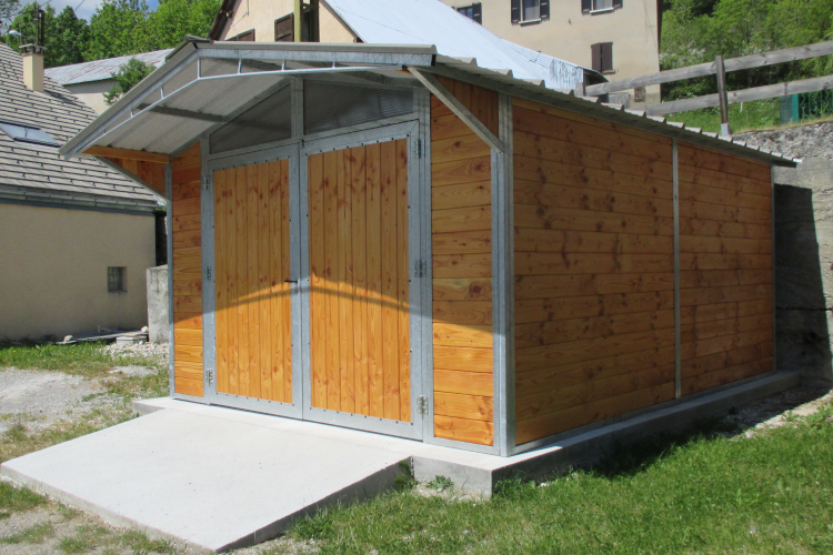 Un garage à armature métallique et habillage bois est posé sur une dalle béton.